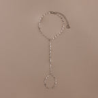 The Sparkle Hand Chain Bracelet features delicate silver mirror-cut links and a graceful finger loop, beautifully showcased against a neutral beige background.