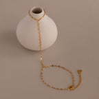 The Sparkle Hand Chain Bracelet, featuring delicate mirror-cut gold links, is elegantly draped over a small round white vase on a neutral background.
