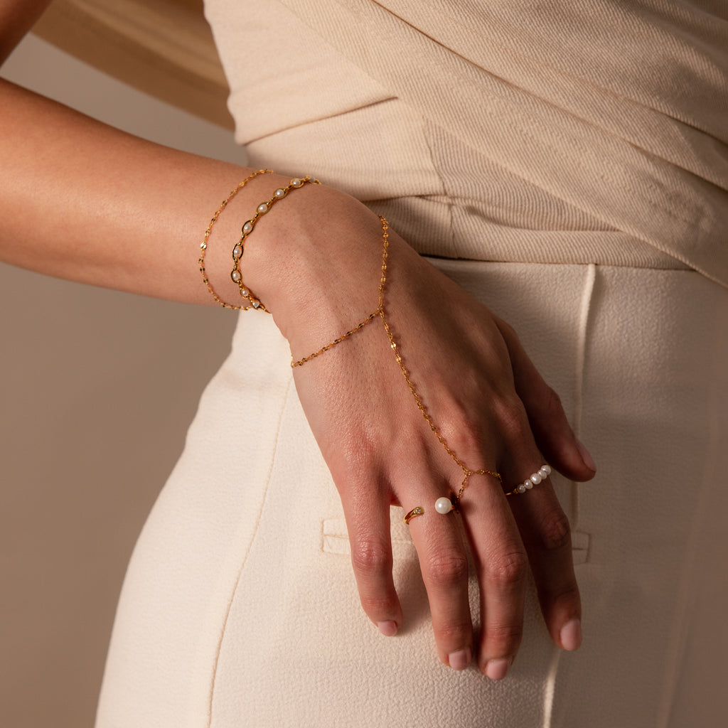 A hand wearing the Sparkle Hand Chain Bracelet rests on the hip of a person dressed in cream-colored pants.