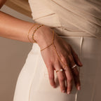 A hand wearing the Sparkle Hand Chain Bracelet rests on the hip of a person dressed in cream-colored pants.
