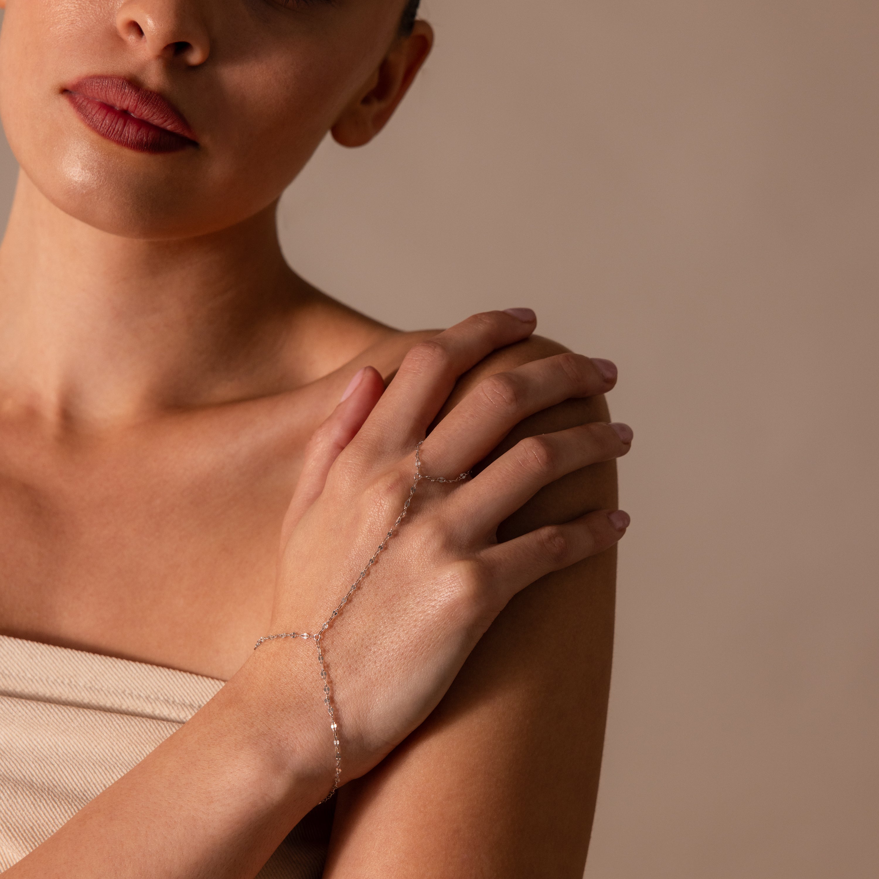 A woman wears the Sparkle Hand Chain Bracelet in Silver, its mirror-cut links glimmering as she gently crosses her hands over her shoulder.