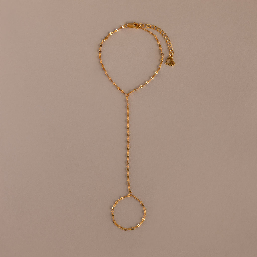 The Sparkle Hand Chain Bracelet in 18K Gold features mirror-cut links and an adjustable clasp, shown on a beige background.