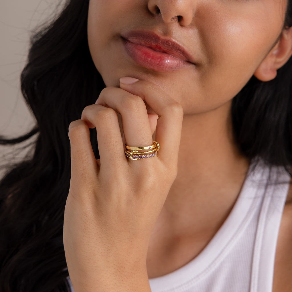 A woman in a white tank top touches her face, showcasing a sparkling Triple Linked Birthstone Ring Set on her finger.