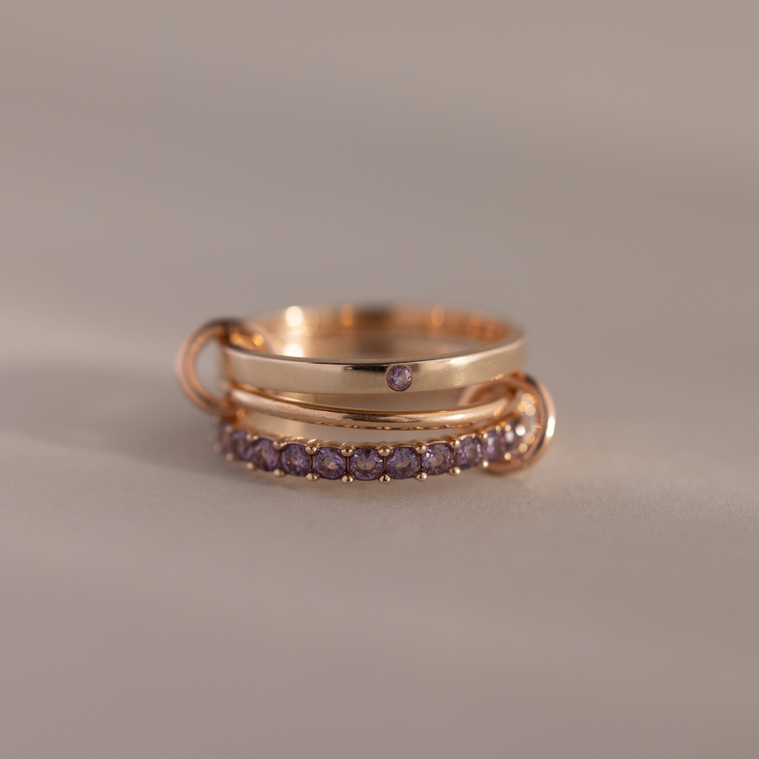 Triple Linked Alexandrite Ring Set featuring gold bands and small purple alexandrite gemstones, stacked on a neutral background.