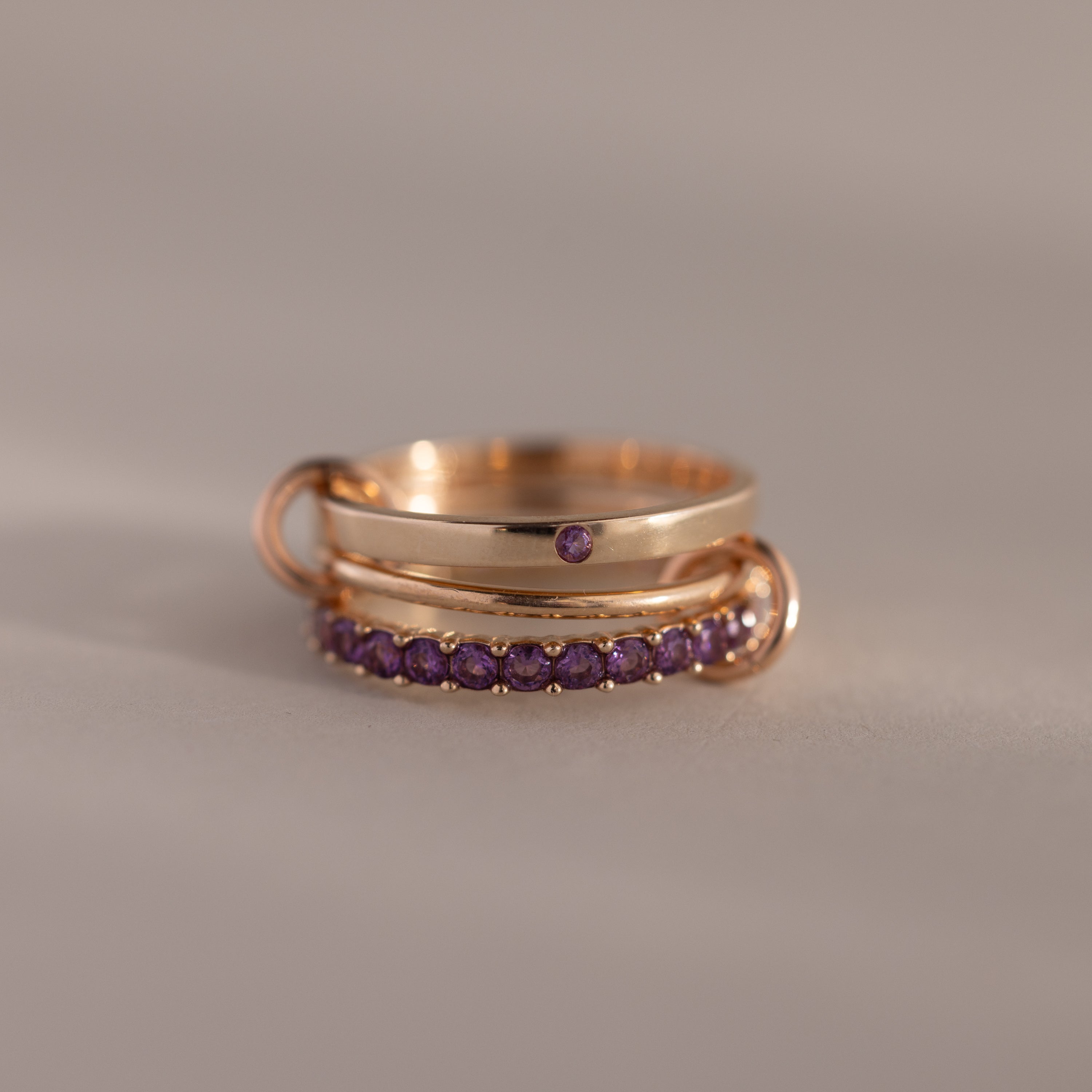 Triple Linked Amethyst Ring Set featuring small purple stones on linked gold bands, displayed on a neutral background.