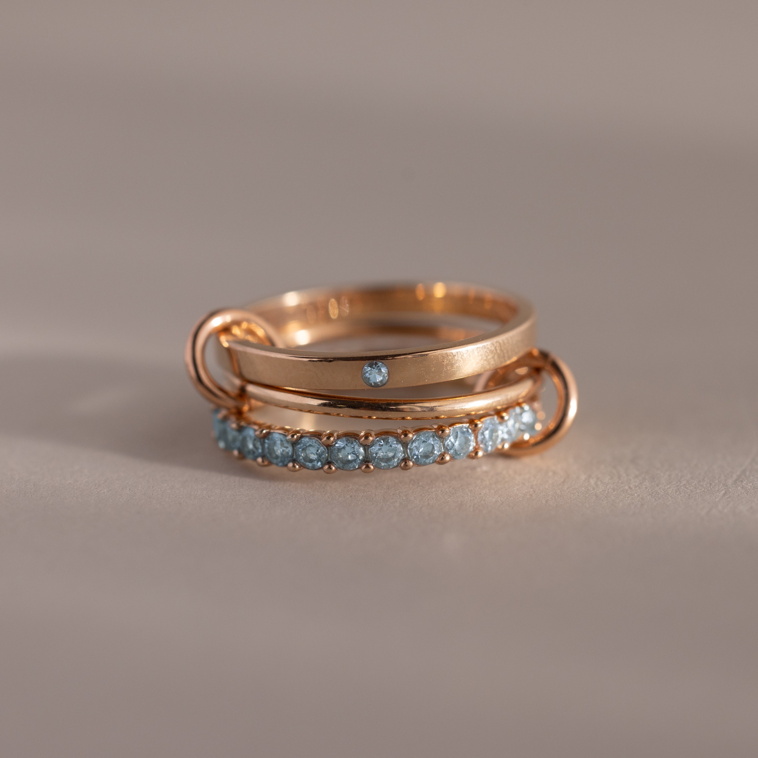 The Triple Linked Aquamarine Ring Set, featuring rose gold bands adorned with aquamarine stones, is stacked together on a neutral background.