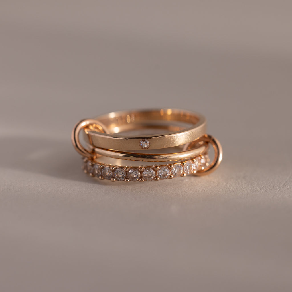 The Triple Linked Diamond Ring Set, featuring an elegant statement ring with multiple diamonds and a delicate band with a small diamond, is stacked on a neutral surface.