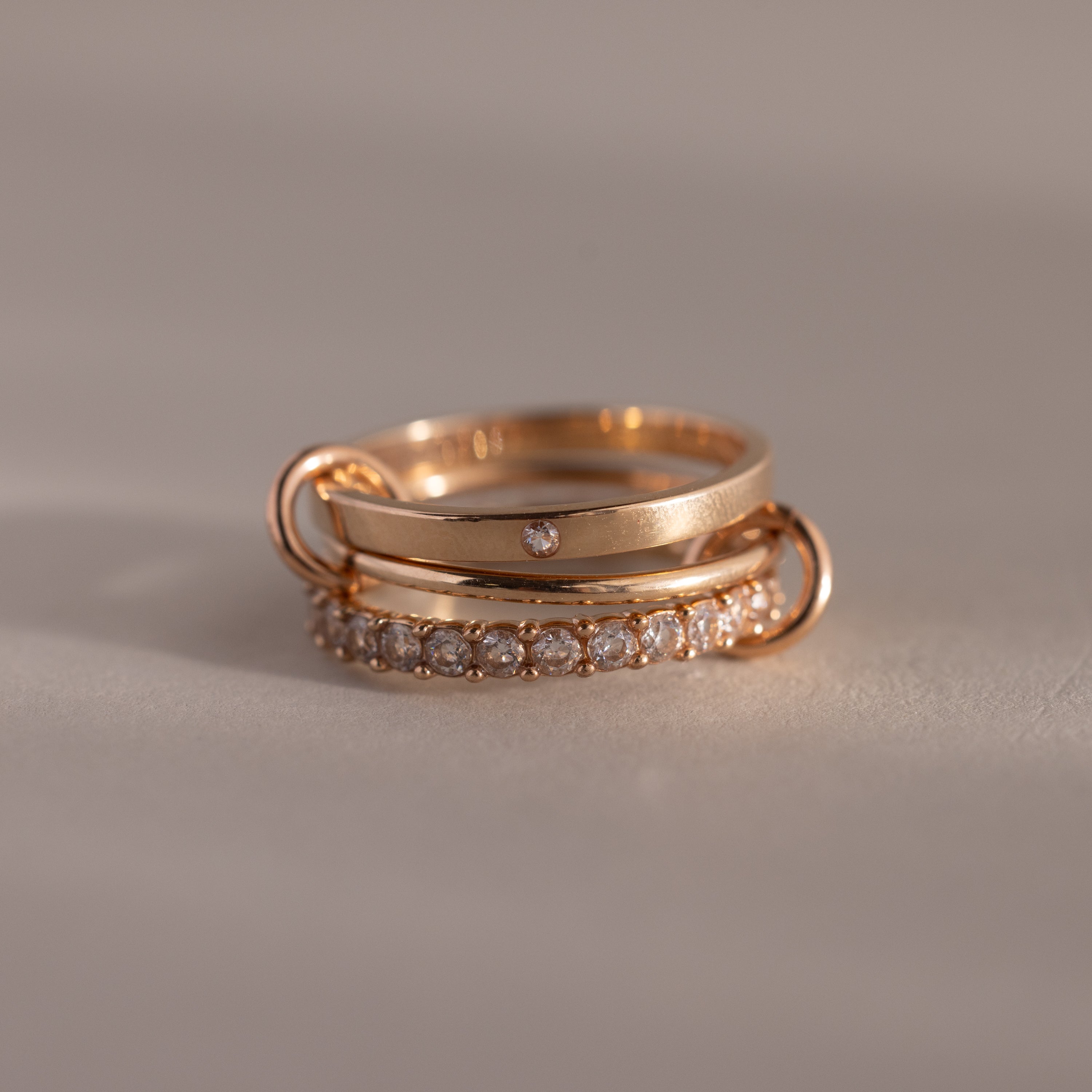 The Triple Linked Diamond Ring Set, featuring an elegant statement ring with multiple diamonds and a delicate band with a small diamond, is stacked on a neutral surface.