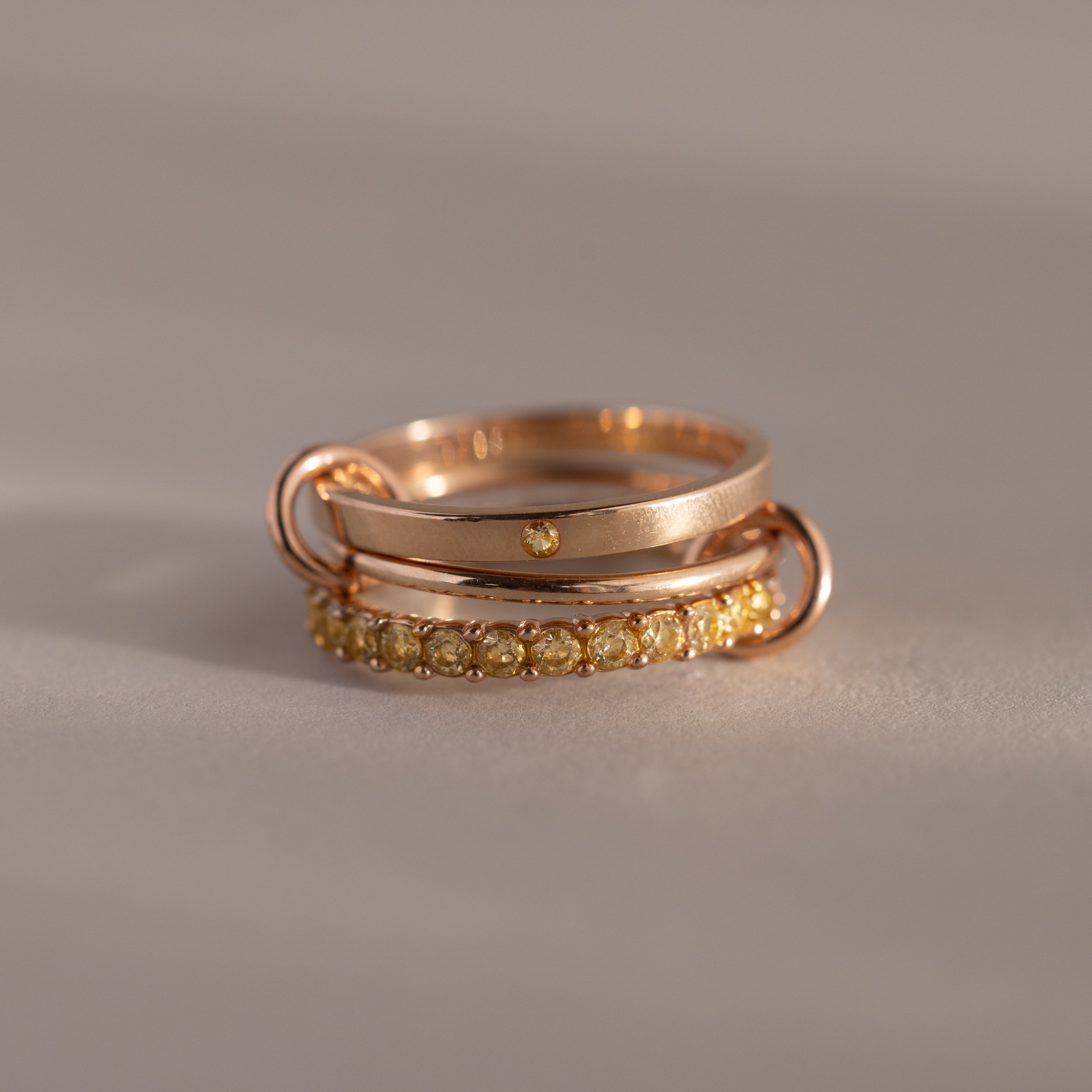 The Triple Linked Topaz Ring Set features three stacked gold rings: one plain, one with a small gem, and one eternity band adorned with yellow topaz stones.