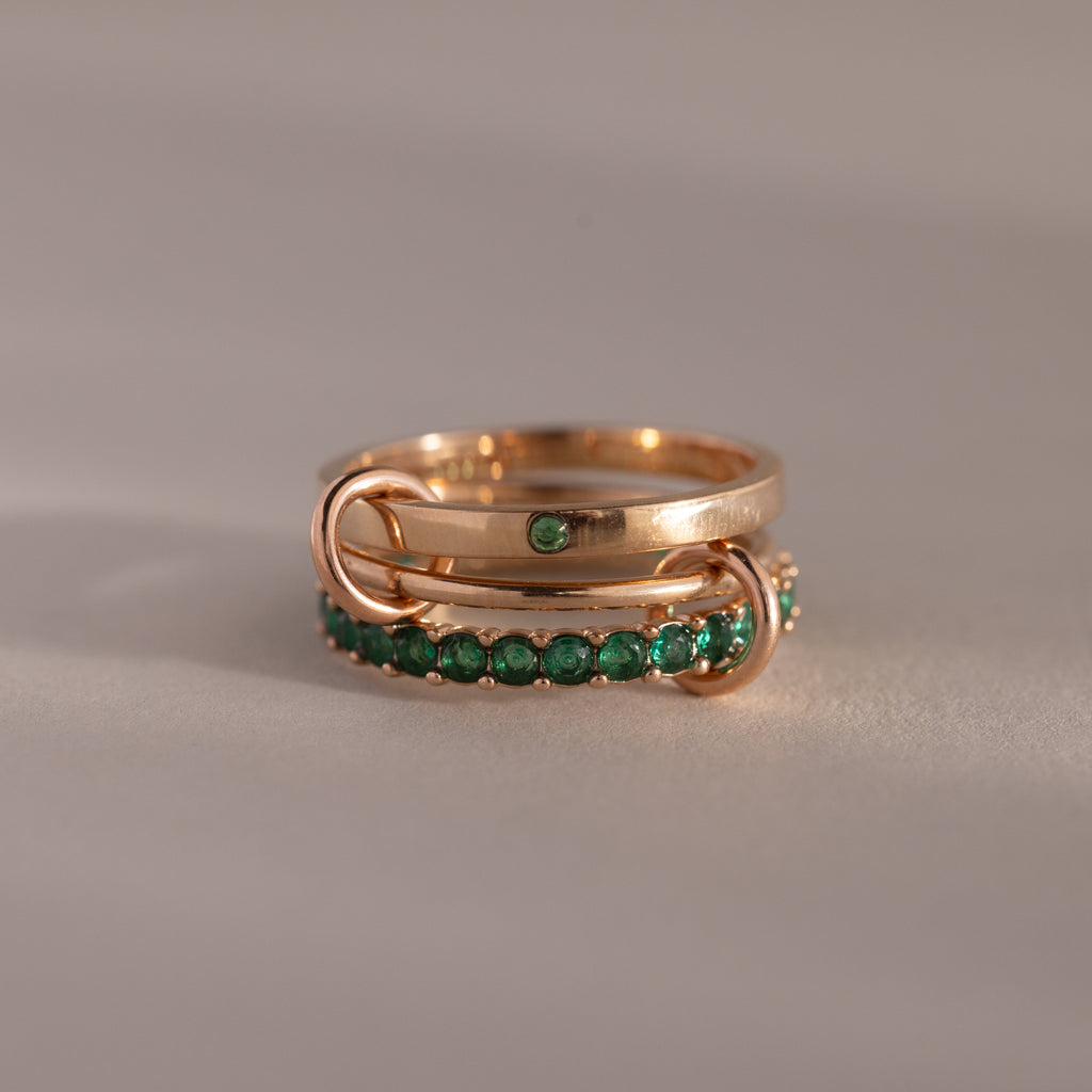 The Triple Linked Emerald Ring Set features three gold rings linked together—one plain with a green gem and two adorned with small green stones—creating a bold statement piece.