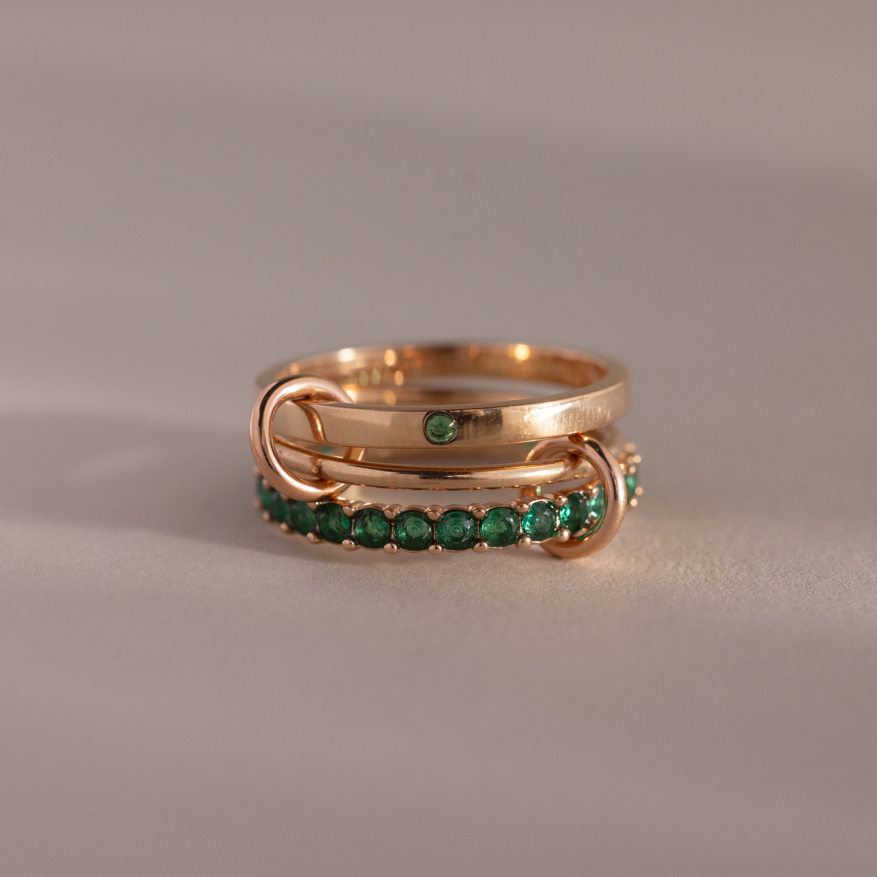 The Triple Linked Emerald Ring Set features three gold rings linked together—one plain with a green gem and two adorned with small green stones—creating a bold statement piece.
