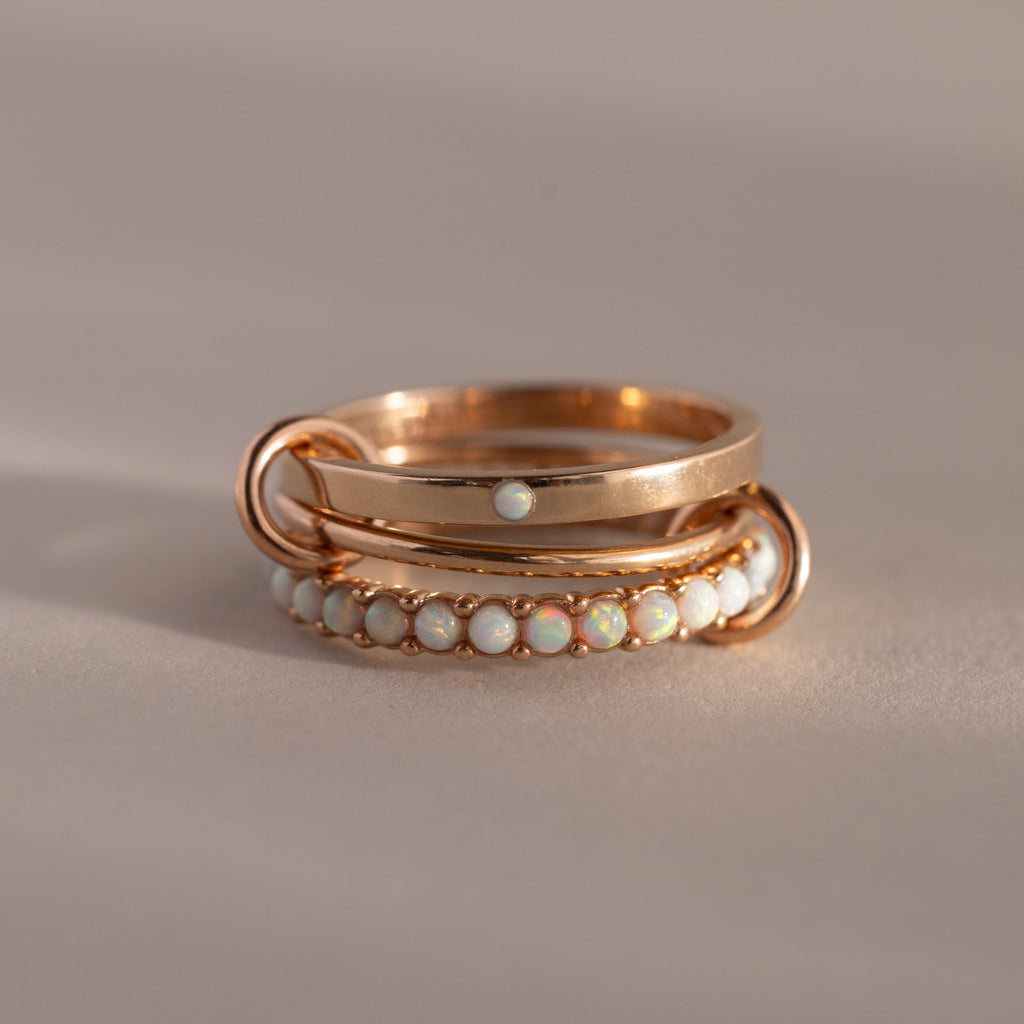 The Triple Linked Opal Ring Set features elegant gold rings with opal stones, beautifully displayed on a neutral beige background.