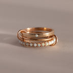 The Triple Linked Opal Ring Set features elegant gold rings with opal stones, beautifully displayed on a neutral beige background.