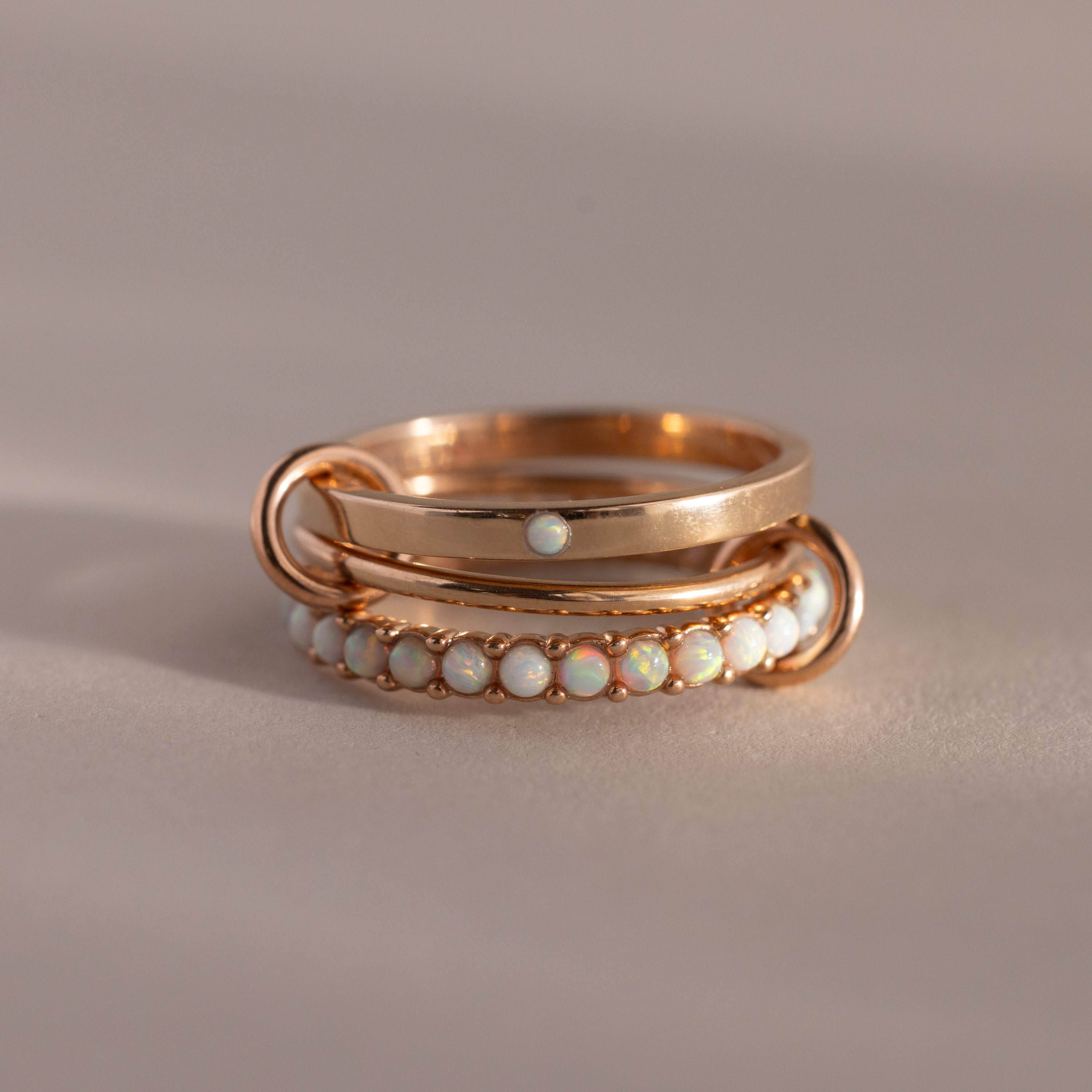The Triple Linked Opal Ring Set features elegant gold rings with opal stones, beautifully displayed on a neutral beige background.