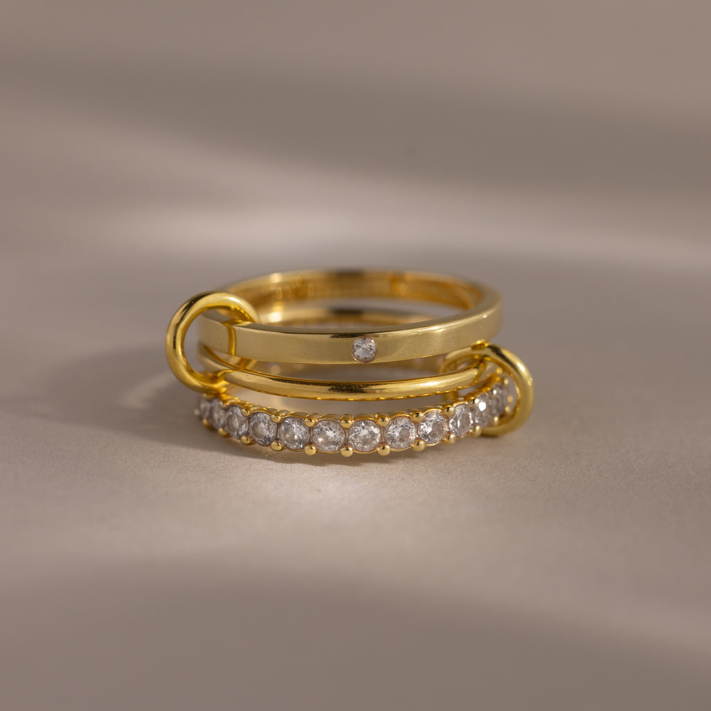 The Triple Linked Diamond Ring Set, featuring a statement ring with a row of small diamonds and a plain band with a single diamond, is displayed elegantly on a neutral background.