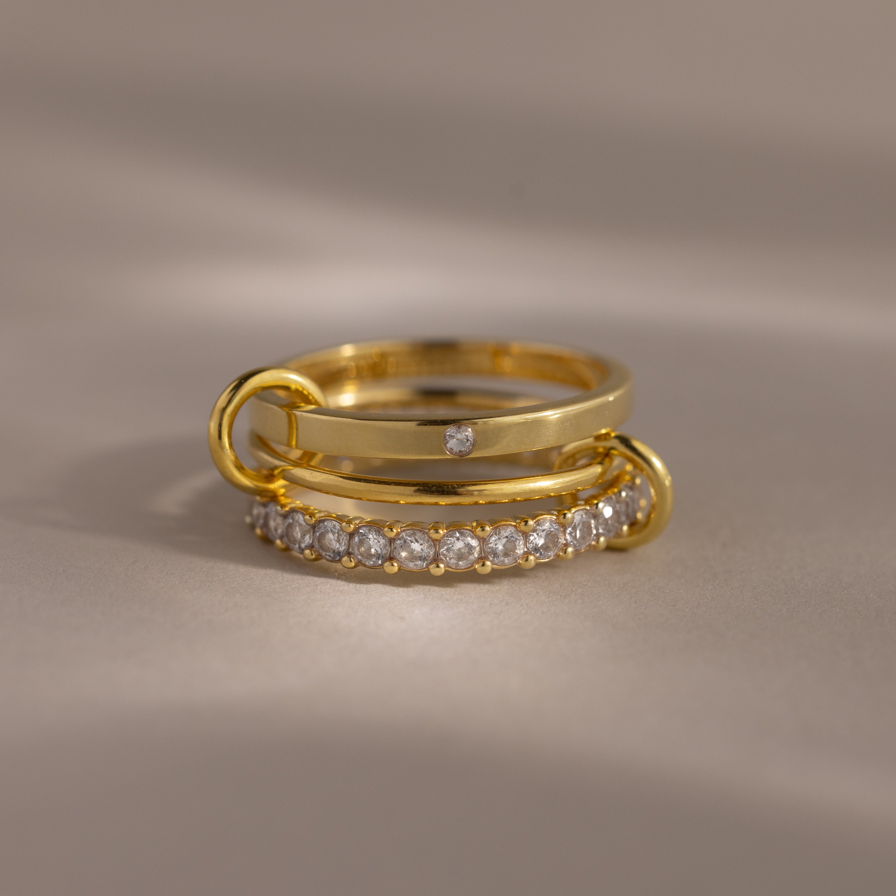 The Triple Linked Diamond Ring Set, featuring a statement ring with a row of small diamonds and a plain band with a single diamond, is displayed elegantly on a neutral background.