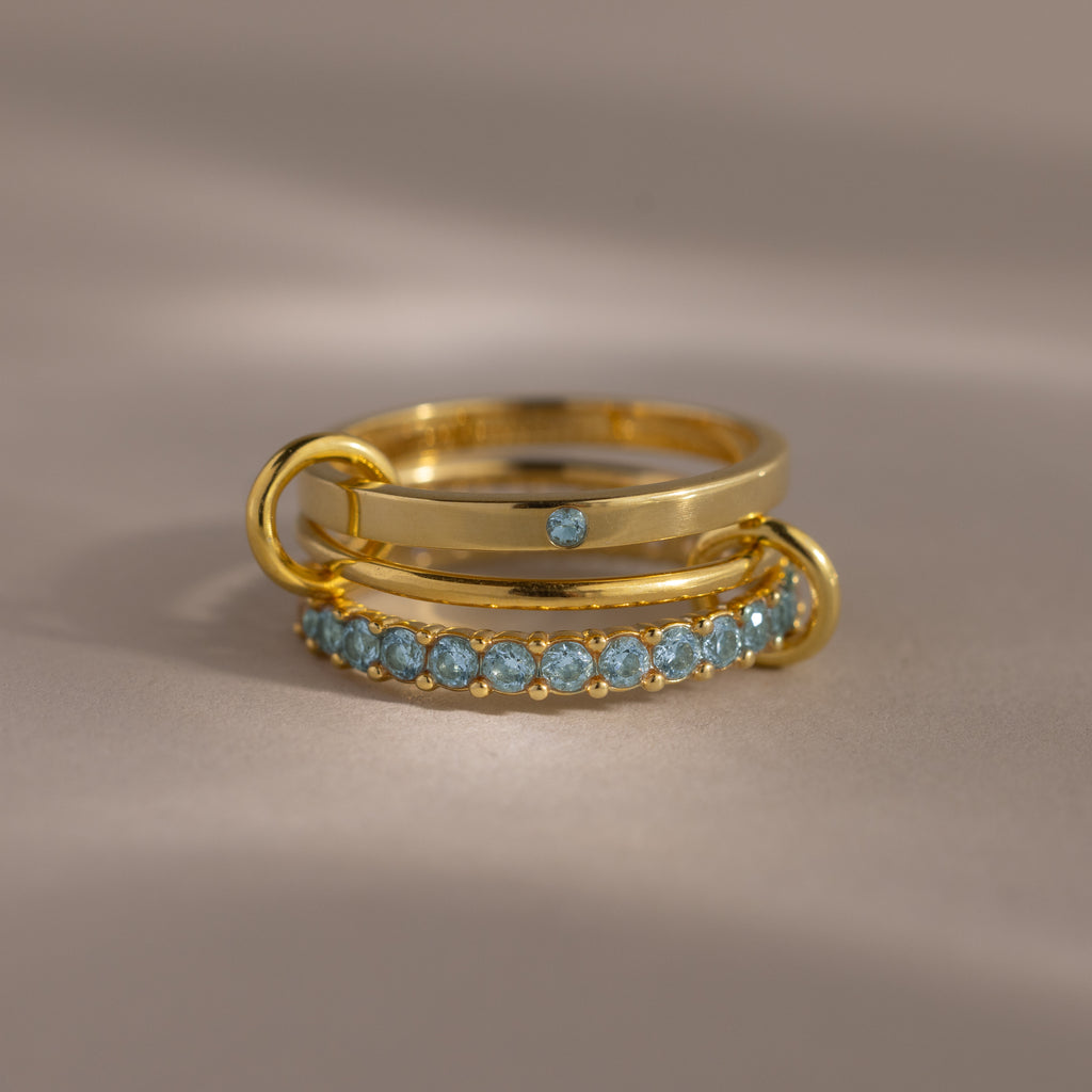 The Triple Linked Aquamarine Ring Set features beautifully stacked gold rings, including a statement piece with a blue stone and a band adorned with aquamarine gems.