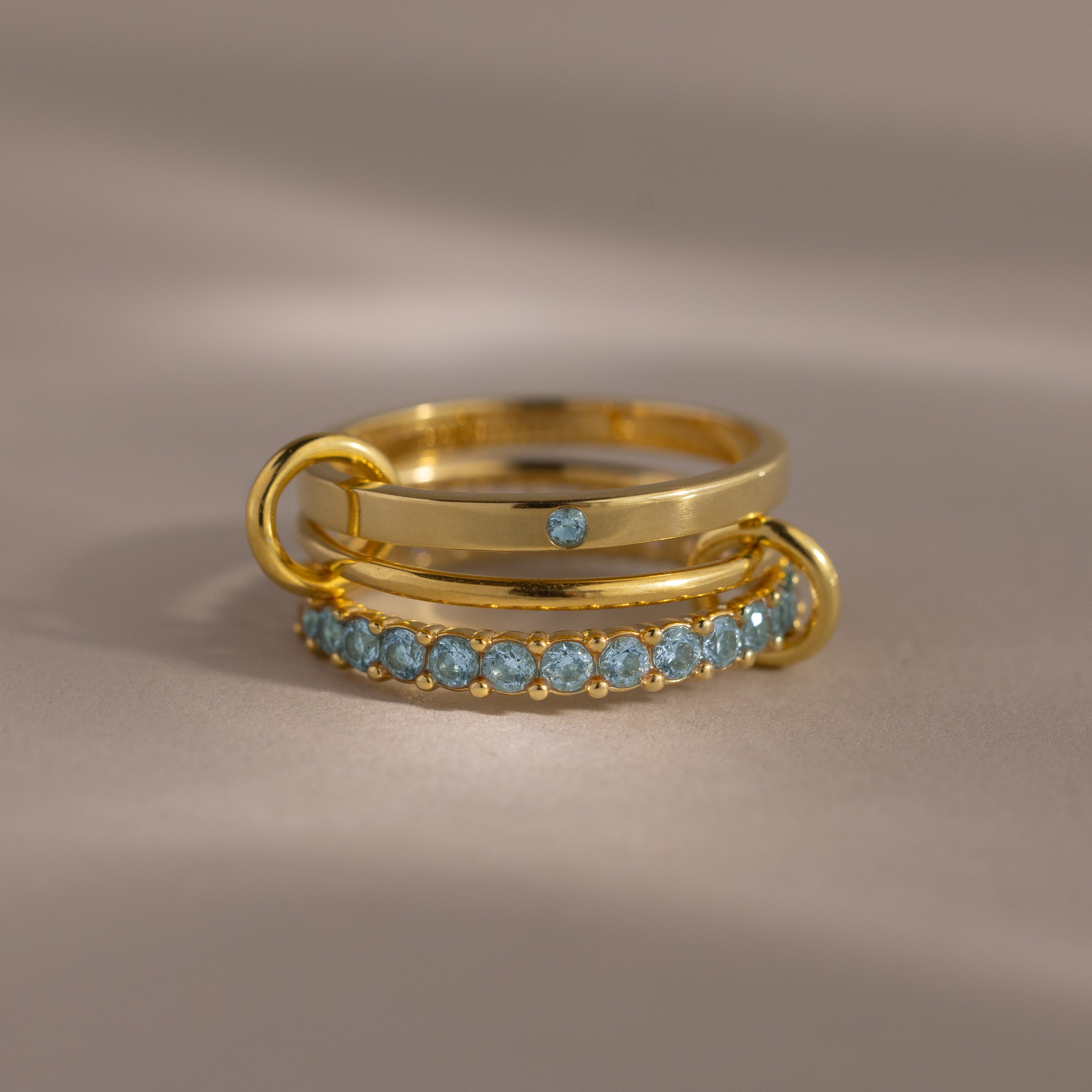 The Triple Linked Aquamarine Ring Set features beautifully stacked gold rings, including a statement piece with a blue stone and a band adorned with aquamarine gems.