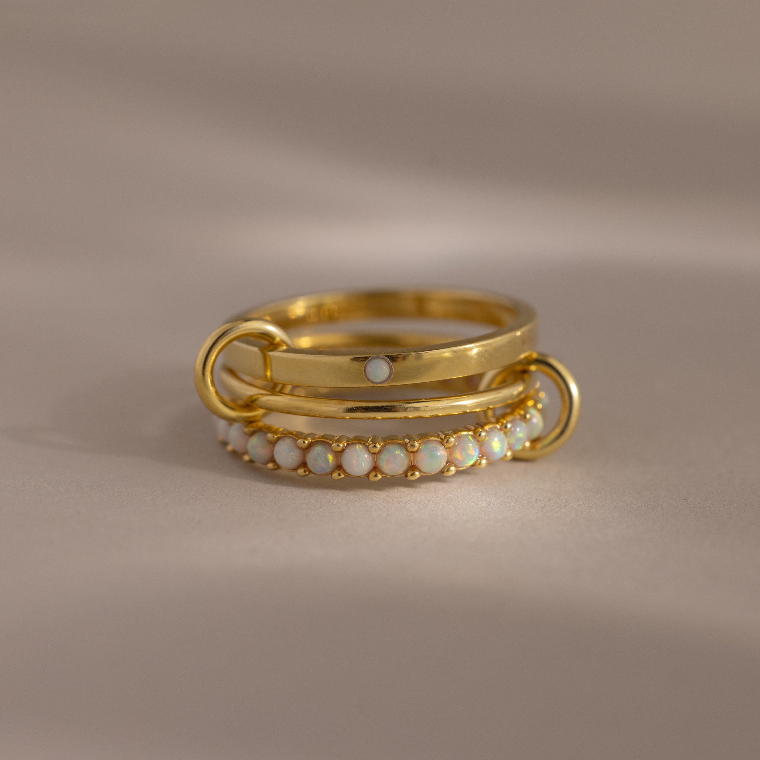 The Triple Linked Opal Ring Set features three stacked gold rings—one with delicate pearl-like beads and another with a sparkling white opal—for an elegant, layered look.