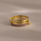 The Triple Linked Birthstone Ring Set in Alexandrite (June) features three gold rings, one accented with purple stones, stacked on a neutral background—a gorgeous set for any occasion.