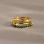 The Triple Linked Emerald Ring Set features two stacked gold rings: an eternity band with green stones and a statement ring with a single green stone, beautifully displayed on a neutral background.