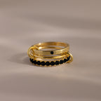 The Triple Linked Onyx Ring Set, featuring stacked gold rings with shimmering black stones, is displayed on a neutral background.