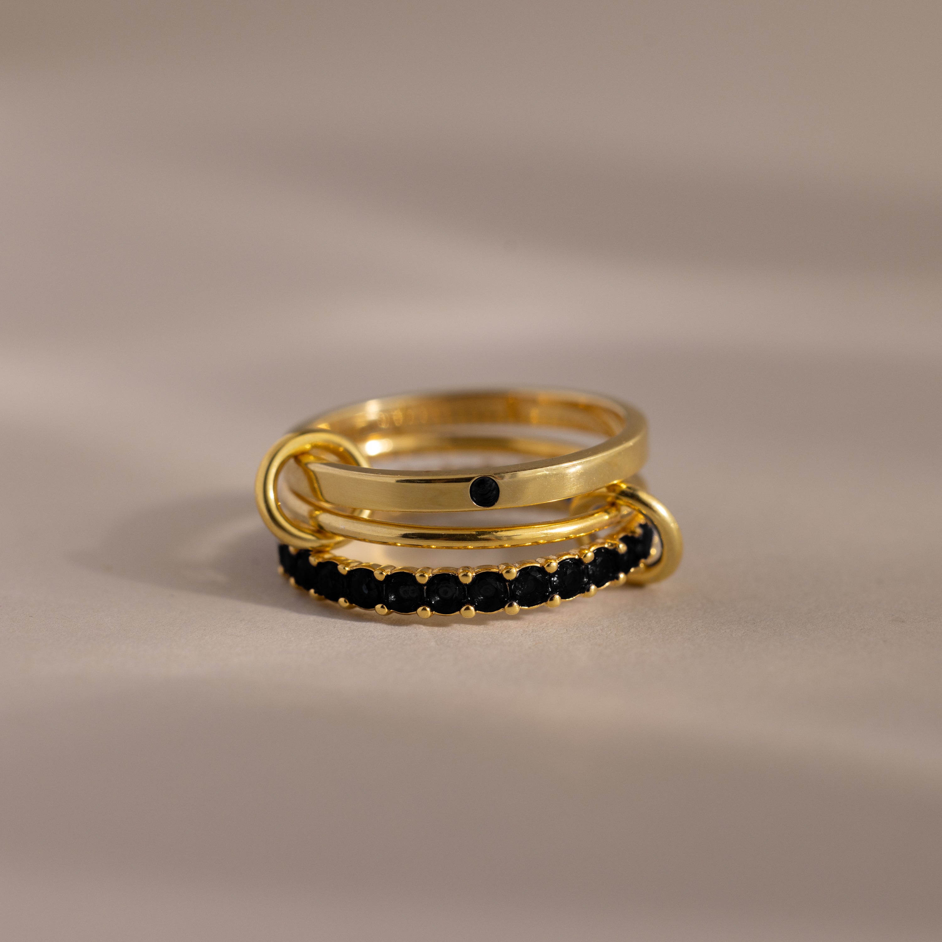 The Triple Linked Onyx Ring Set, featuring stacked gold rings with shimmering black stones, is displayed on a neutral background.