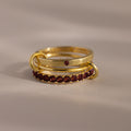 The Triple Linked Garnet Ring Set, featuring gold rings with red gemstones, is stacked together on a neutral surface under soft lighting.