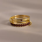 The Triple Linked Garnet Ring Set, featuring gold rings with red gemstones, is stacked together on a neutral surface under soft lighting.