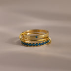 The Triple Linked Blue Zircon Ring Set, featuring gold bands with blue zircon stones, is stacked together on a neutral surface under soft lighting.
