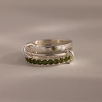 The Triple Linked Peridot Ring Set features three silver rings interlocked, with one adorned by green peridot gemstones, creating a striking birthstone ring set displayed against a neutral background.