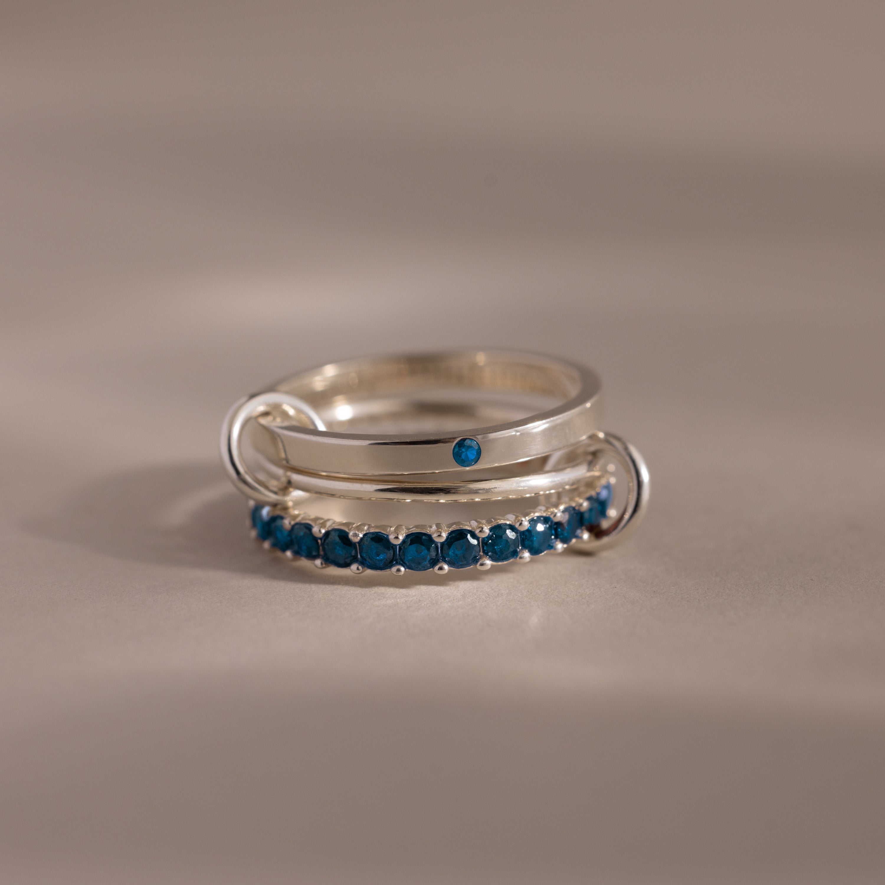 The Triple Linked Blue Zircon Ring Set features a plain band with a single blue zircon stone and an eternity band adorned with a row of sparkling blue zircons.