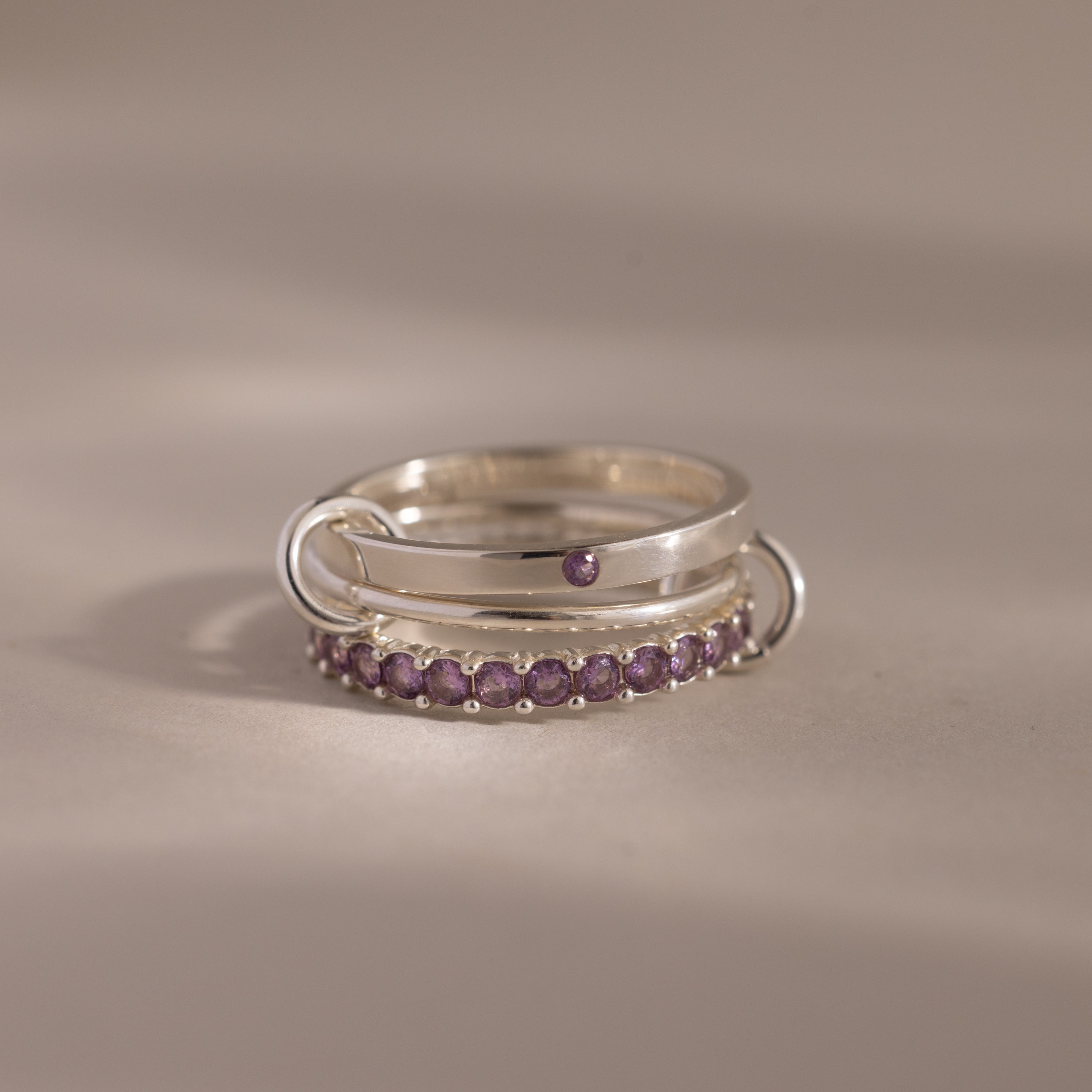 Triple Linked Alexandrite Ring Set featuring small purple gemstones and two metallic loops, displayed on a neutral background.