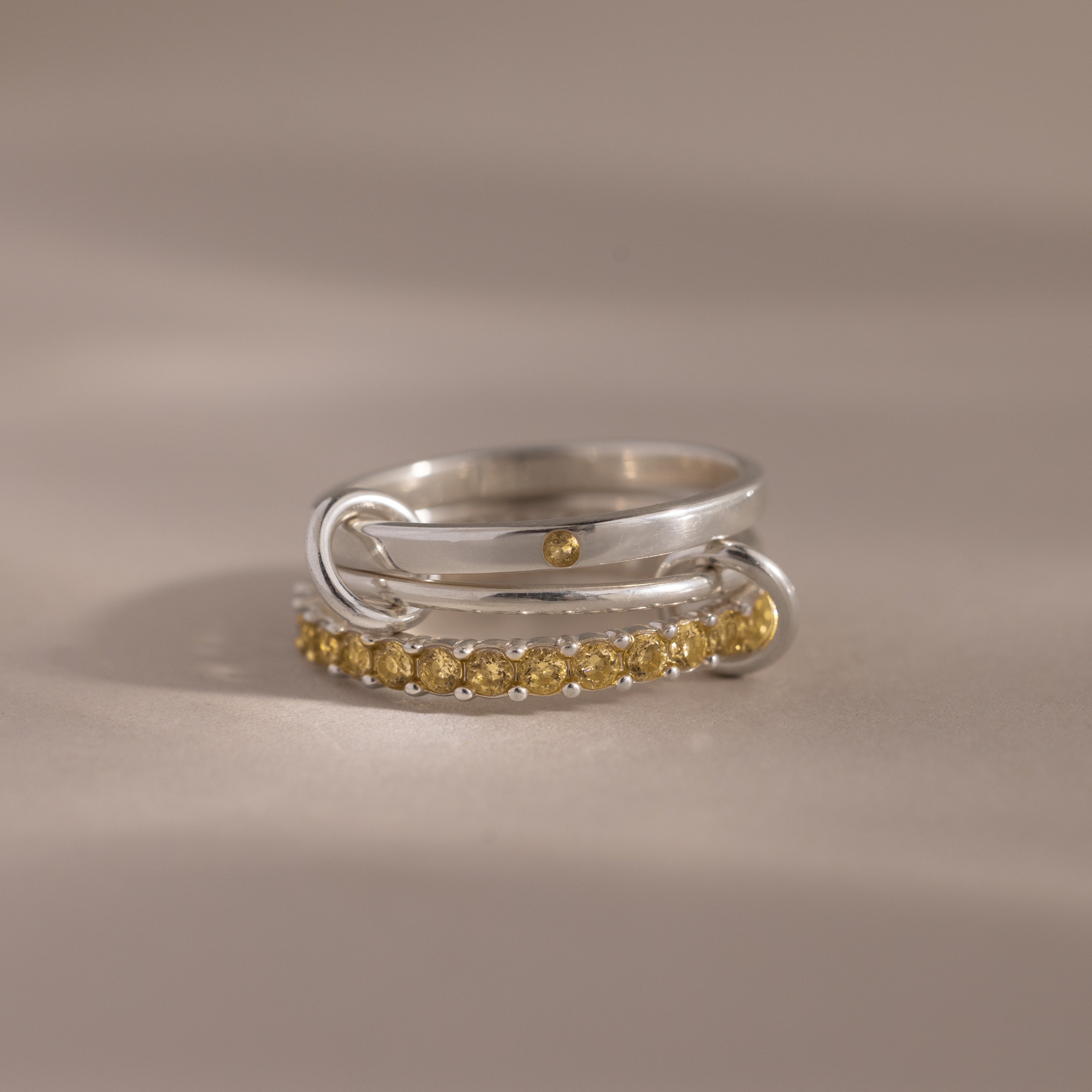 The Triple Linked Topaz Ring Set features a silver ring with a small gold dot, connected to a gold-studded band, creating a modern statement piece against a neutral background.
