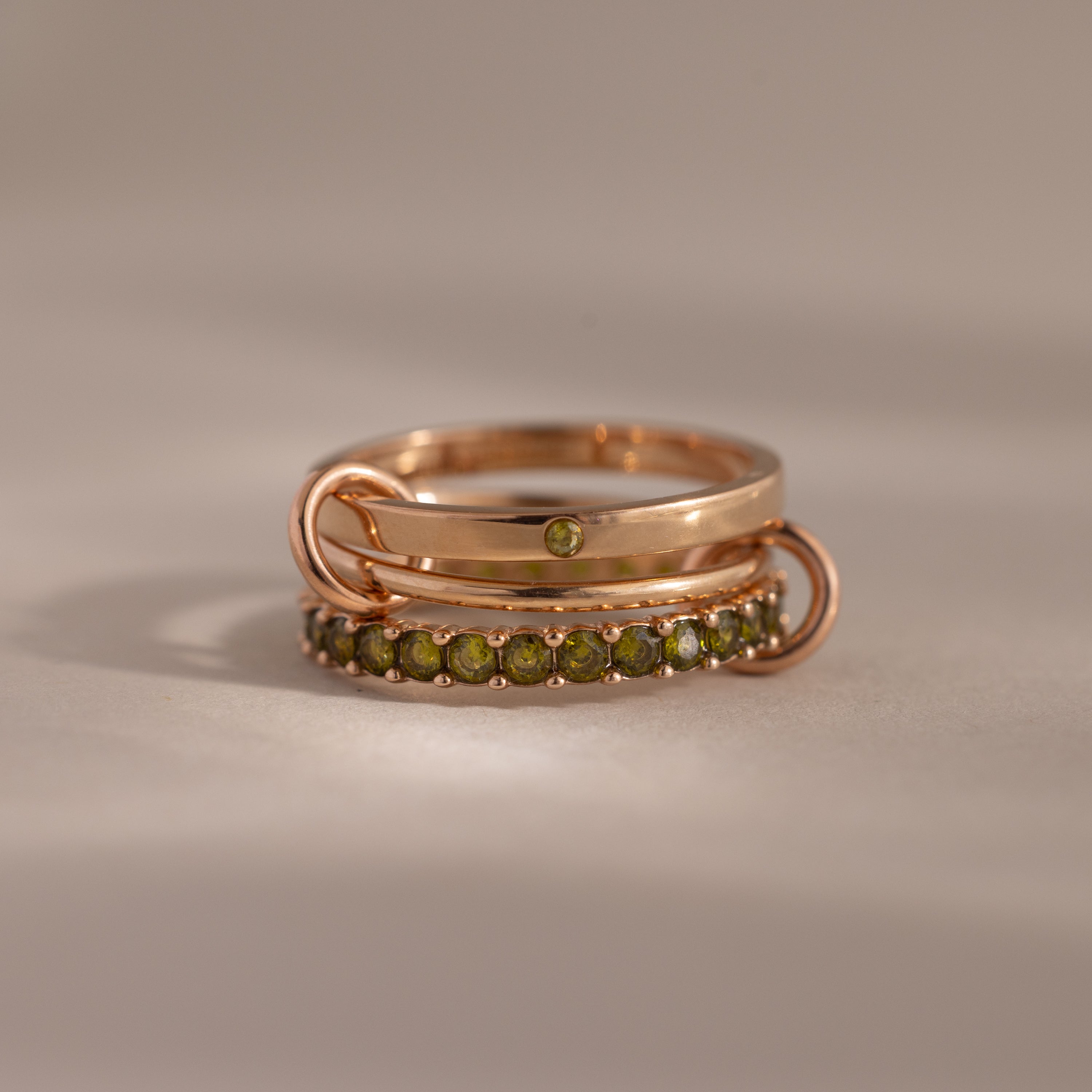 The Triple Linked Peridot Ring Set features two rose gold rings with green gemstones, elegantly stacked together on a neutral background.