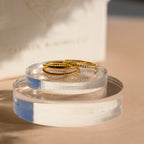 Two Thin Stacking Rings from our 18K Gold Set rest on clear acrylic stands in soft, natural light—a stylish ring stack and perfect Christmas gift.