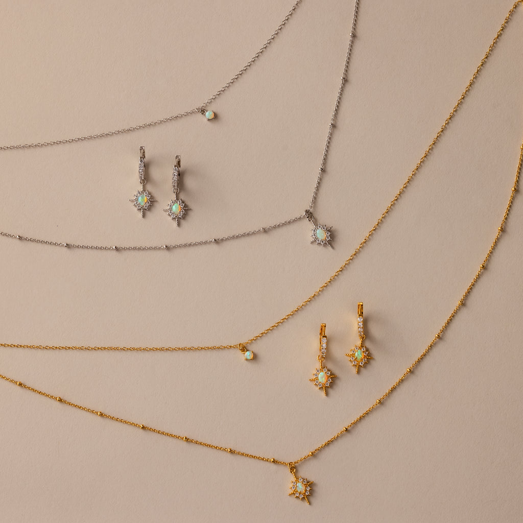 The Opal Star Necklace & Earrings Set in 18K Gold, featuring gold and silver star designs, is beautifully displayed on a beige background.