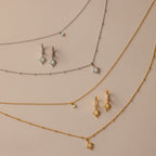 The Opal Star Necklace & Earrings Set in 18K Gold, featuring gold and silver star designs, is beautifully displayed on a beige background.