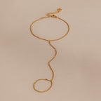 Delicate curb hand chain bracelet in 18K gold resting on a neutral surface.