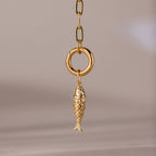 Gold fish charm pendant with intricate scale detailing, hanging from a polished circular link on a chain.