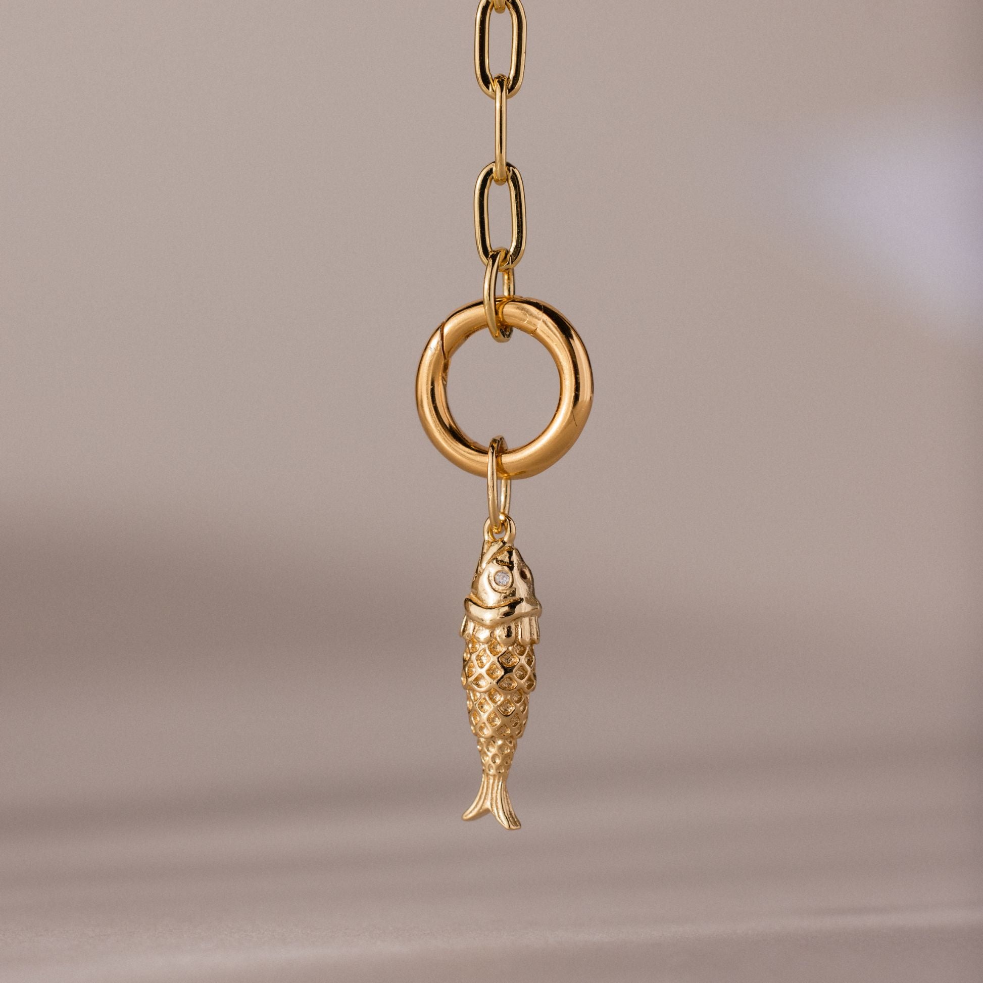 Gold fish charm pendant with intricate scale detailing, hanging from a polished circular link on a chain.