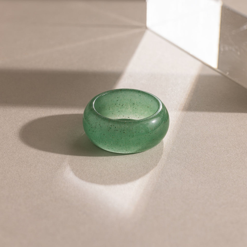 Close-up of a thick green jade gemstone statement ring with a smooth, glossy finish, displayed on a neutral surface.