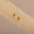 Dainty gold cross stud earrings displayed on a neutral ribbon fabric.