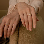 Close-up of two hands on a chair, each adorned with the Baguette Diamond Ring in an elegant east-west bezel setting.