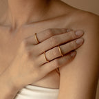 A hand adorned with the Minimal Stacking Ring and two gold bands rests gently on a bare shoulder against a neutral backdrop.