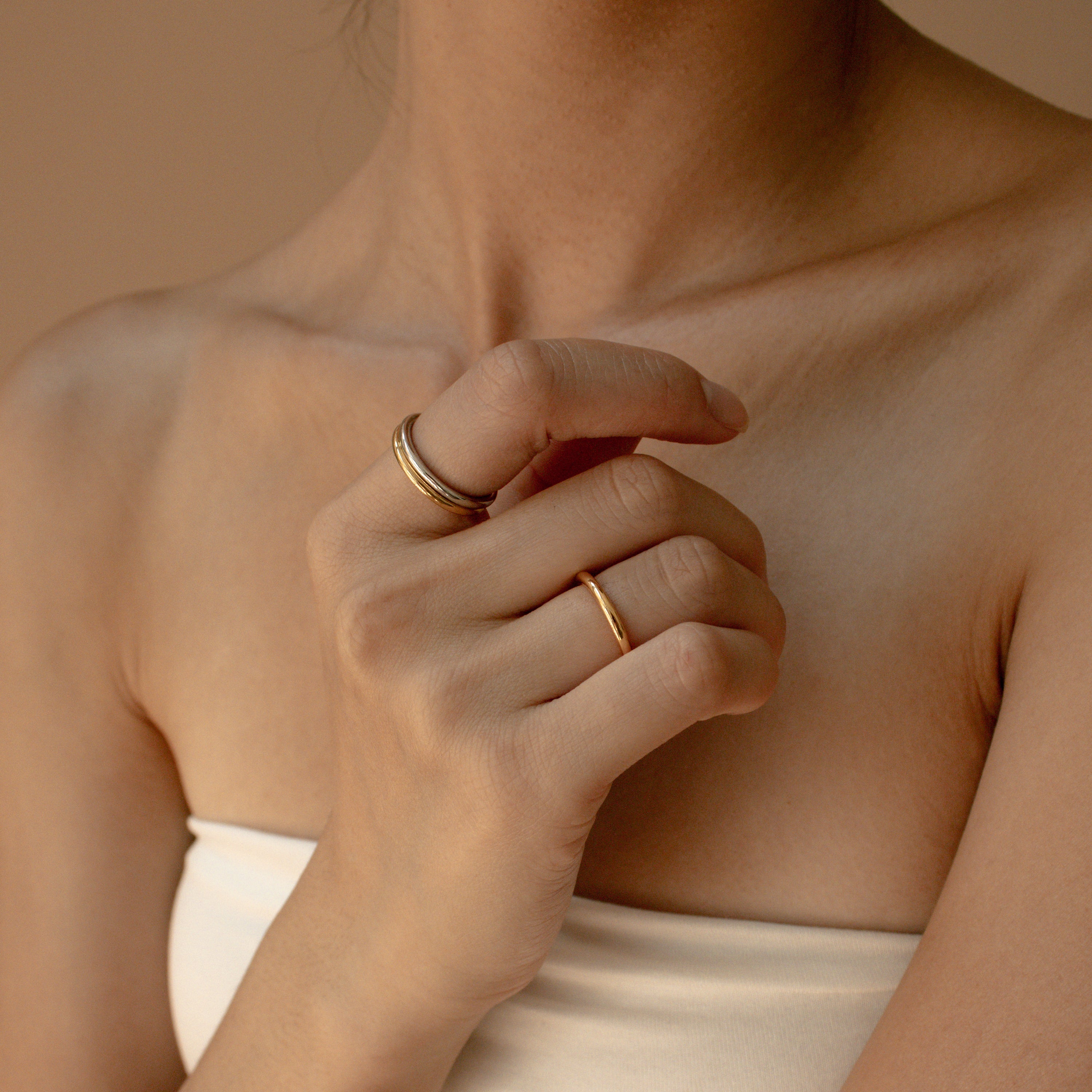A woman wearing the Minimal Stacking Ring in gold poses with her hand near her collarbone, styled in a white bandeau top.