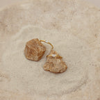Two Baguette Diamond Rings with delicate baguette diamonds in an east-west bezel setting, displayed on rocks in a sand-filled dish.