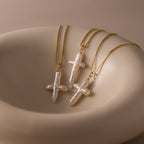 Three Baroque Pearl Cross Necklaces are displayed on a smooth, cream dish, adding a minimalist touch to any style.