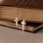 Two Baroque Pearl Cross Necklaces—one with a silver chain, one with a gold chain—are displayed on stacked books, offering a perfect minimalist look.