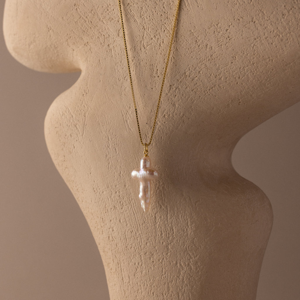 Baroque Pearl Cross Necklace in 18K Gold displayed on a beige textured mannequin bust.